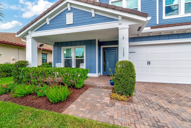 entrance to property with board and batten siding, covered porch, a tile roof, and a garage