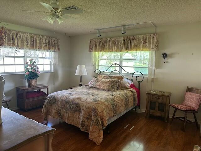 bedroom featuring multiple windows, ceiling fan, dark hardwood / wood-style flooring, and a textured ceiling