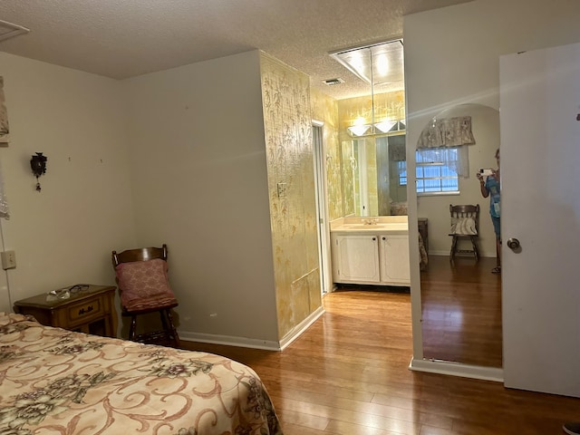 bedroom with a textured ceiling, light hardwood / wood-style floors, ensuite bath, and sink