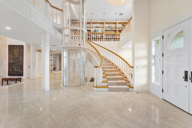 entryway featuring a towering ceiling, decorative columns, stairs, and baseboards