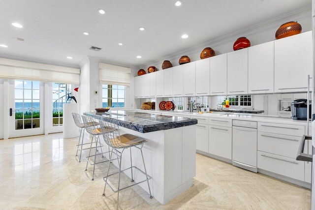 kitchen featuring visible vents, white cabinets, a center island, a kitchen bar, and crown molding