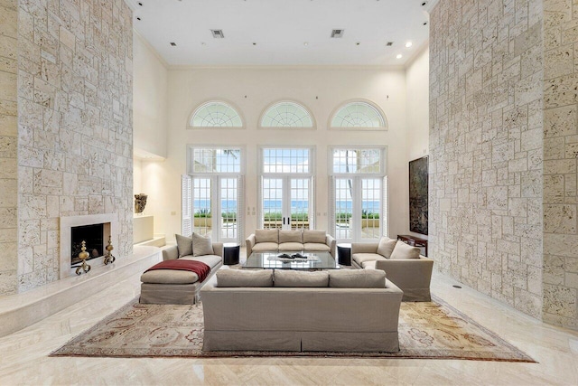 living room with crown molding, french doors, a high ceiling, and a stone fireplace