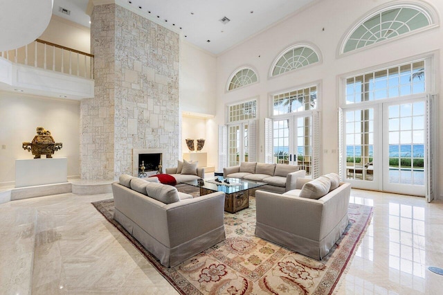 living room featuring a water view, a high ceiling, crown molding, a stone fireplace, and french doors