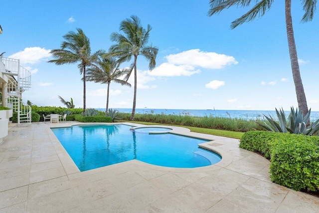 view of swimming pool featuring a pool with connected hot tub, a water view, a patio, and stairs