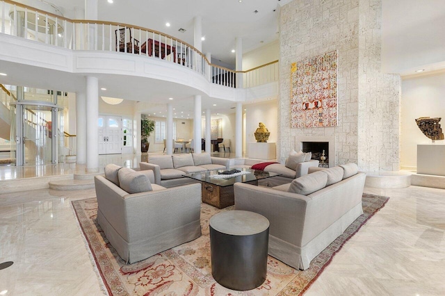 living area featuring a fireplace, a towering ceiling, marble finish floor, stairway, and decorative columns