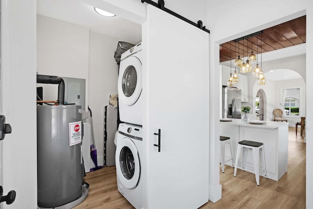 clothes washing area with light wood-type flooring, a barn door, stacked washer / dryer, wood ceiling, and water heater