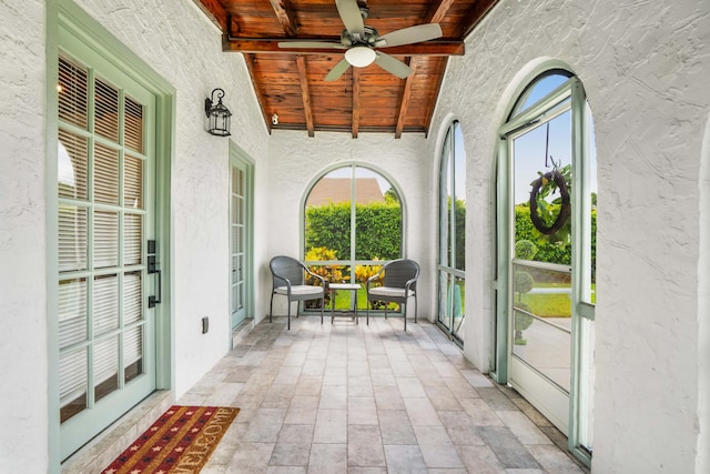 unfurnished sunroom featuring wood ceiling, beamed ceiling, and ceiling fan