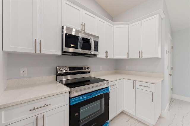 kitchen featuring light stone counters, stainless steel appliances, white cabinetry, and vaulted ceiling