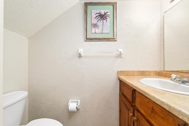 bathroom featuring a textured ceiling, vanity, toilet, and vaulted ceiling