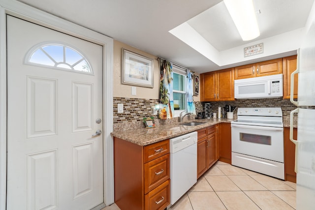 kitchen with backsplash, light tile patterned floors, white appliances, light stone counters, and sink