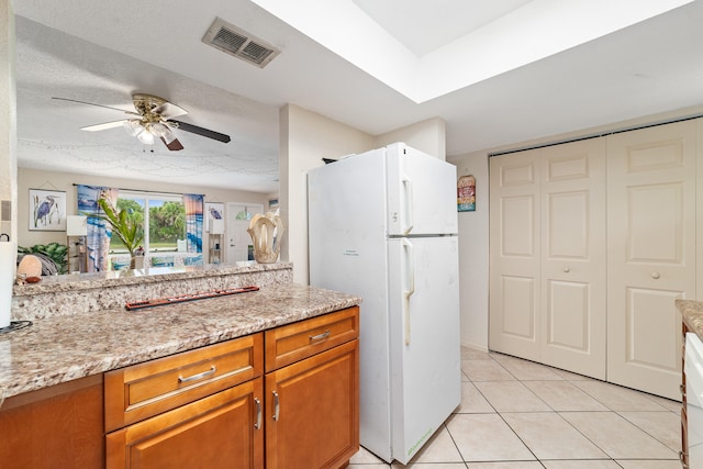 kitchen with a textured ceiling, white fridge, light stone countertops, light tile patterned floors, and ceiling fan