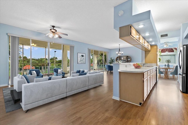 living room featuring ceiling fan with notable chandelier, wood-type flooring, and a textured ceiling