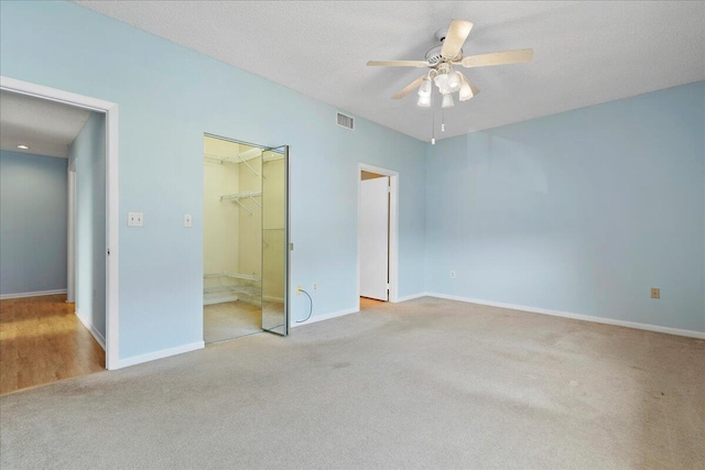 unfurnished bedroom with a spacious closet, ceiling fan, light carpet, a textured ceiling, and a closet