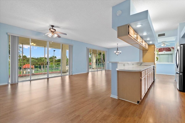 kitchen with hanging light fixtures, sink, ceiling fan with notable chandelier, and stainless steel refrigerator