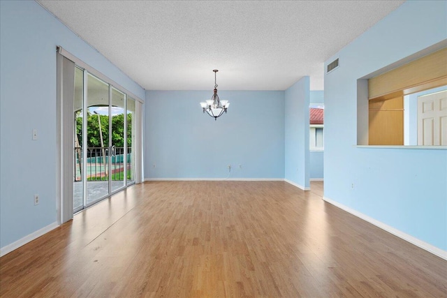 spare room featuring an inviting chandelier, hardwood / wood-style flooring, and a textured ceiling