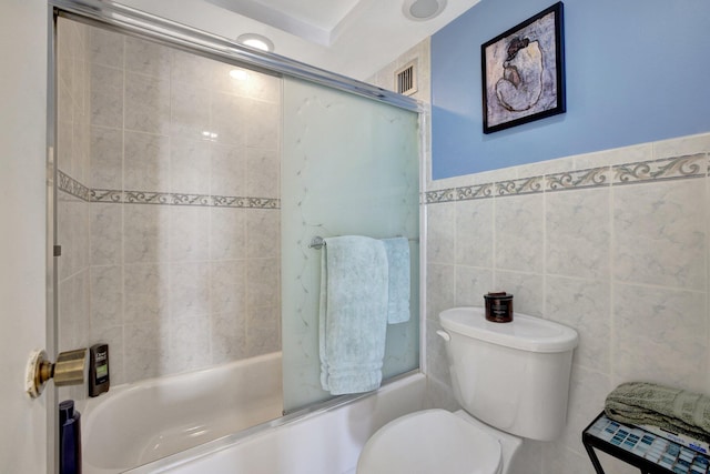 bathroom with tile walls, toilet, and enclosed tub / shower combo