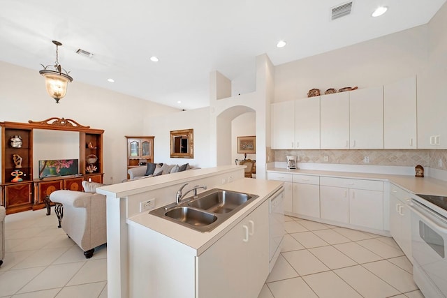 kitchen with an island with sink, backsplash, sink, decorative light fixtures, and white cabinetry