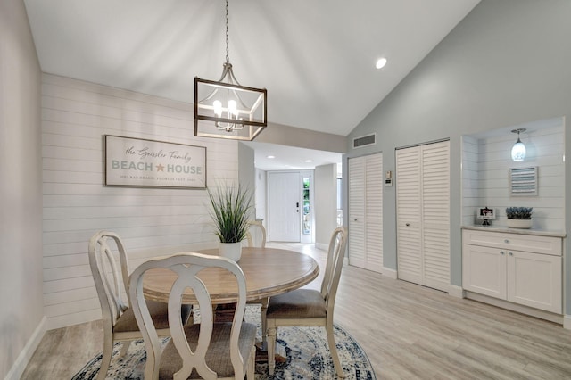 dining space with wood walls, high vaulted ceiling, an inviting chandelier, and light hardwood / wood-style flooring