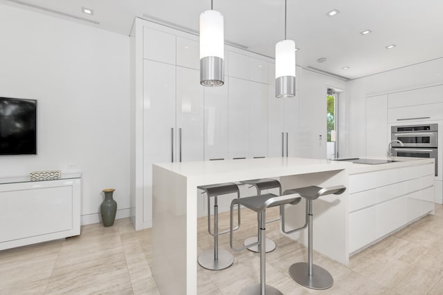 kitchen with pendant lighting, black electric stovetop, stainless steel double oven, white cabinetry, and a center island with sink