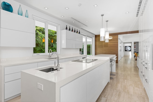 kitchen featuring an island with sink, hanging light fixtures, sink, white cabinetry, and black electric cooktop