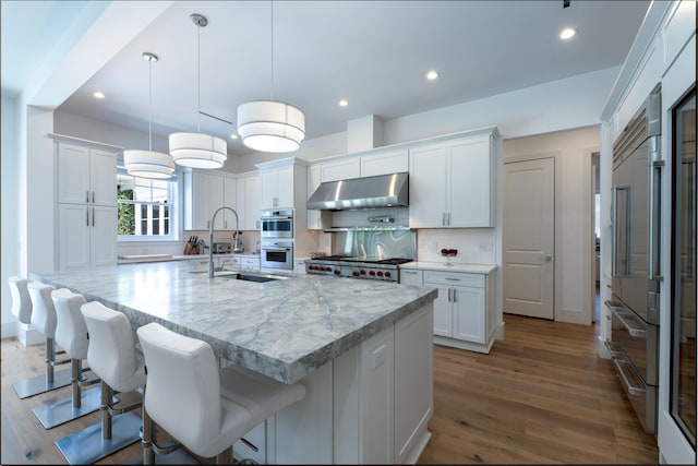 kitchen with a center island with sink, decorative light fixtures, range hood, and white cabinets