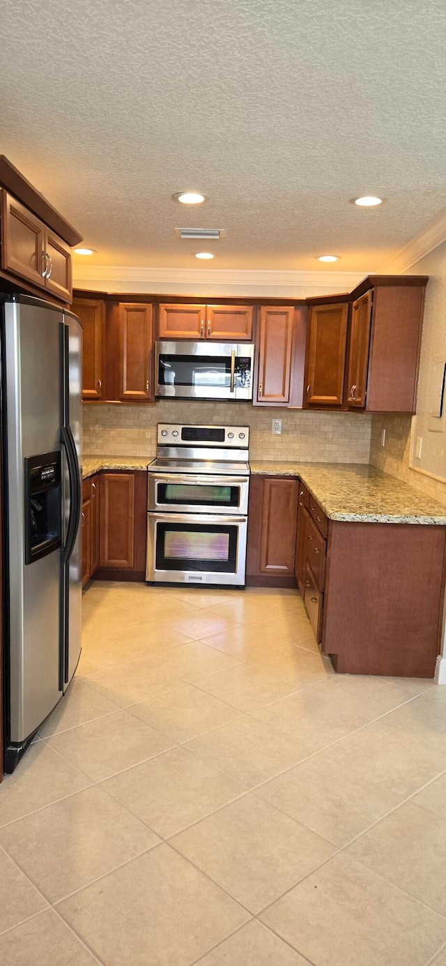 kitchen with a textured ceiling, light stone countertops, light tile patterned floors, appliances with stainless steel finishes, and tasteful backsplash