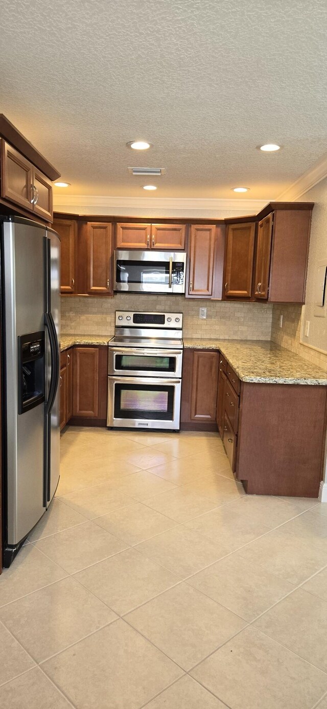 kitchen featuring light tile patterned floors, light stone counters, stainless steel appliances, tasteful backsplash, and a textured ceiling