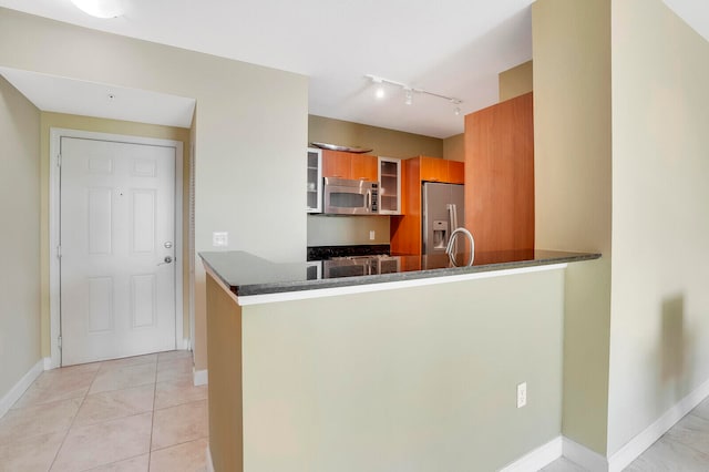 kitchen featuring appliances with stainless steel finishes, kitchen peninsula, light tile patterned floors, and dark stone counters