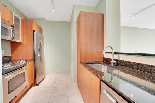 kitchen with dark stone countertops, light tile patterned floors, stainless steel appliances, sink, and track lighting