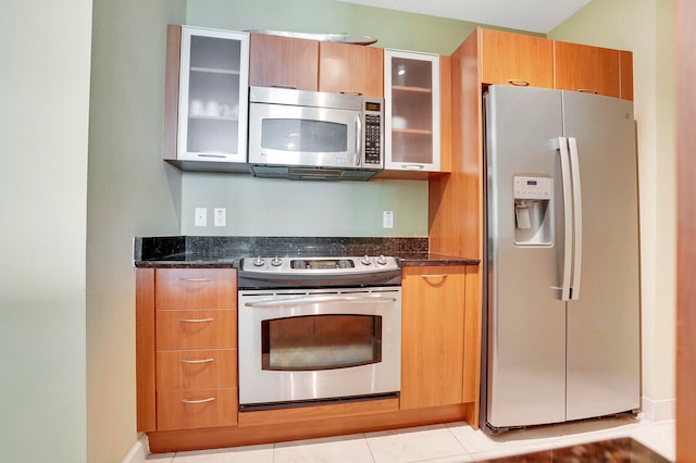 kitchen featuring stainless steel appliances, light tile patterned floors, and dark stone counters