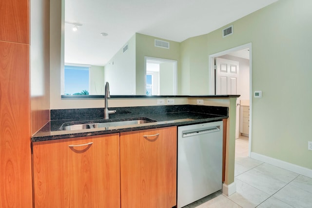 kitchen with stainless steel dishwasher, dark stone countertops, sink, and light tile patterned floors