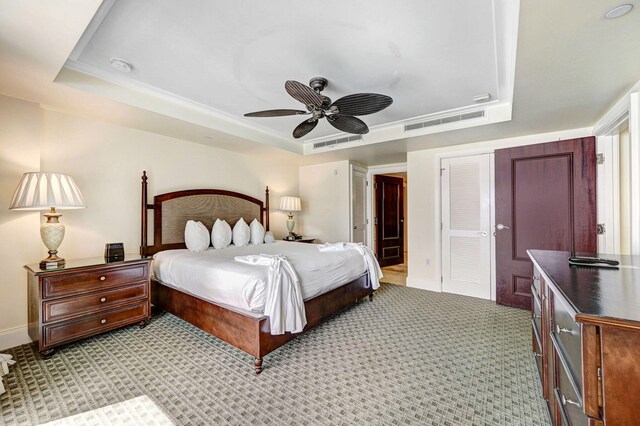 bedroom featuring a raised ceiling, light carpet, and ceiling fan