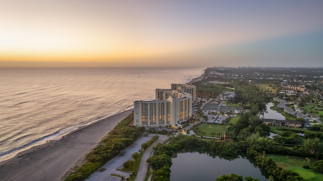 aerial view at dusk featuring a water view and a beach view