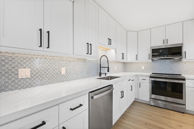 kitchen featuring sink, stainless steel appliances, tasteful backsplash, light stone counters, and light hardwood / wood-style flooring