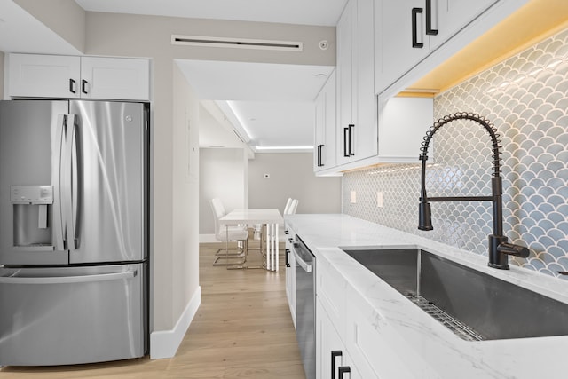 kitchen with appliances with stainless steel finishes, light wood-type flooring, light stone counters, sink, and white cabinets