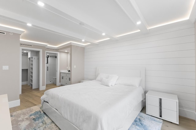 bedroom featuring a walk in closet, light wood-type flooring, ensuite bathroom, and wooden walls