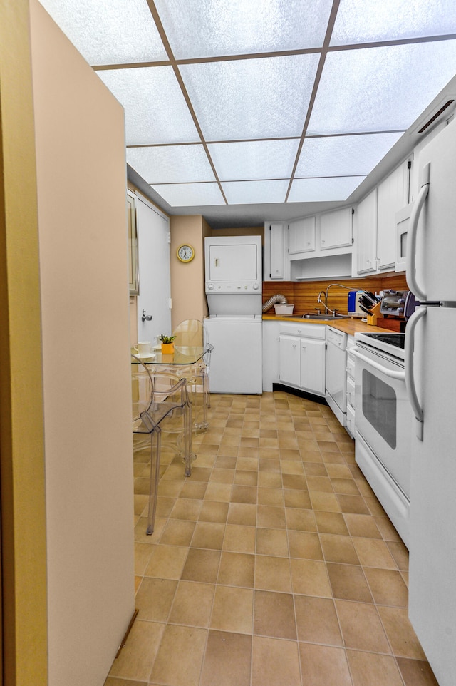 kitchen with white appliances, stacked washing maching and dryer, white cabinetry, a paneled ceiling, and light tile patterned flooring