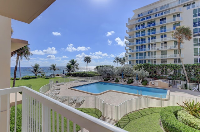 community pool with a patio area, fence, and a water view