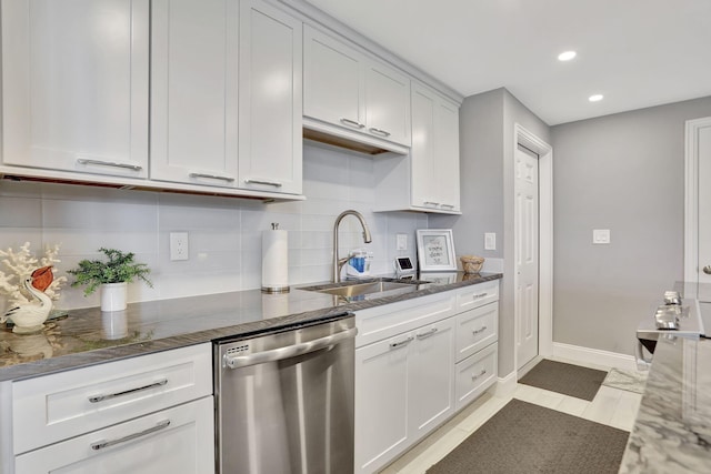 kitchen with a sink, white cabinets, stainless steel dishwasher, decorative backsplash, and dark stone counters