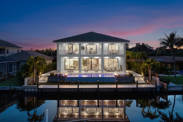 back house at dusk featuring a balcony and a patio area