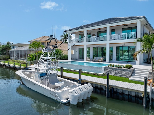 back of property featuring a balcony, a water view, stucco siding, an infinity pool, and a patio area