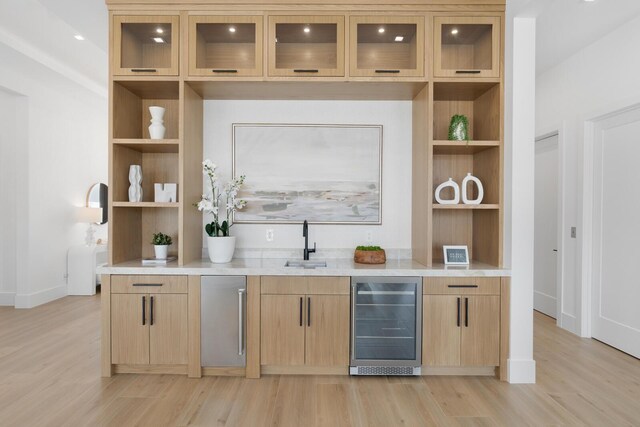 bar with beverage cooler, light brown cabinets, light hardwood / wood-style floors, and sink