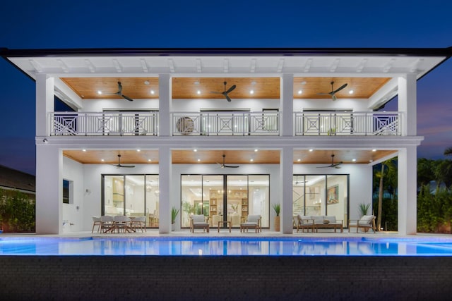 rear view of property featuring an outdoor hangout area, an infinity pool, a balcony, and stucco siding