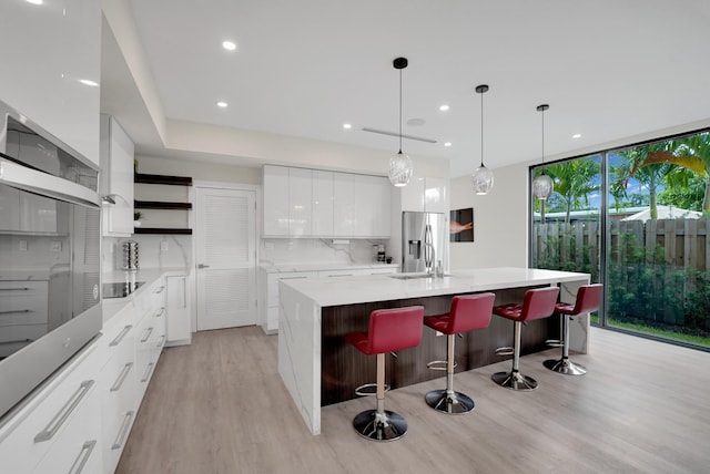 kitchen featuring white cabinets, light wood-type flooring, stainless steel appliances, decorative backsplash, and a kitchen island with sink