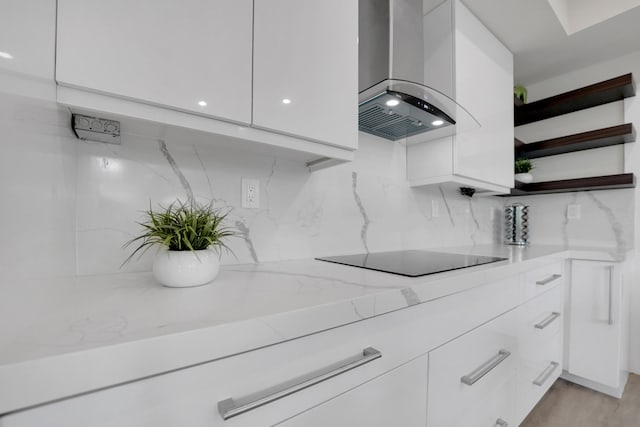 kitchen with wall chimney range hood, black electric cooktop, and white cabinetry