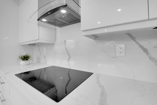 interior details with white cabinetry, black electric cooktop, light stone counters, and wall chimney range hood