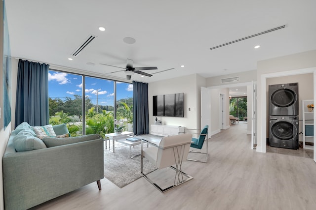 living room with a wealth of natural light, light hardwood / wood-style flooring, ceiling fan, and stacked washer and dryer