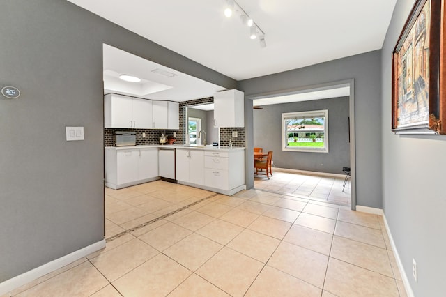 kitchen with decorative backsplash, white dishwasher, sink, light tile patterned floors, and white cabinetry