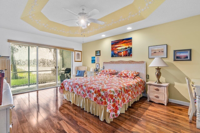 bedroom featuring dark hardwood / wood-style flooring, ceiling fan, a tray ceiling, and access to exterior