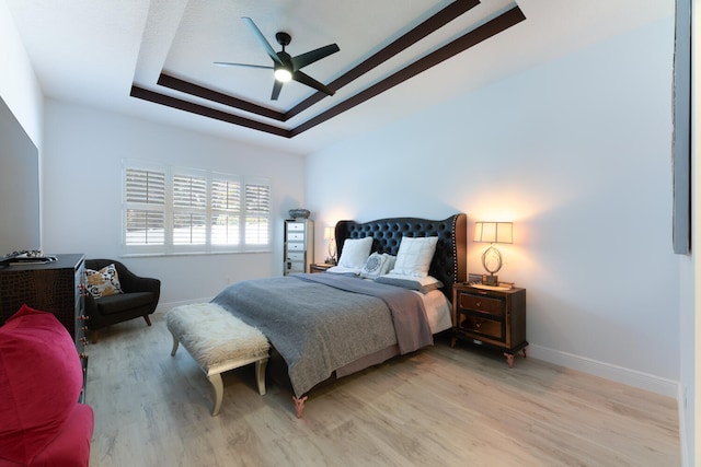 bedroom with light wood finished floors, a raised ceiling, and baseboards